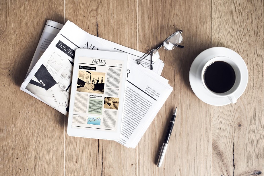 Top view photo of desk with news magazines, pen and coffee.
